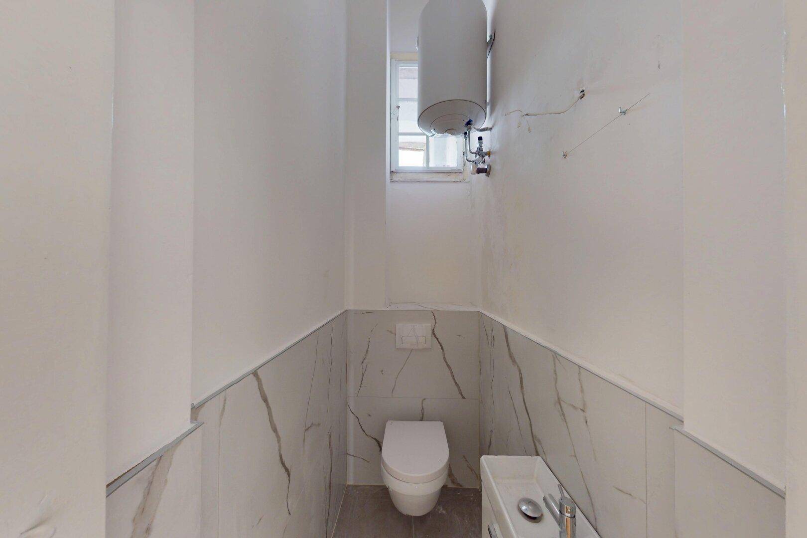 Kleines WC mit wandhängender Toilette, Waschbecken und einem Fenster für Tageslicht.