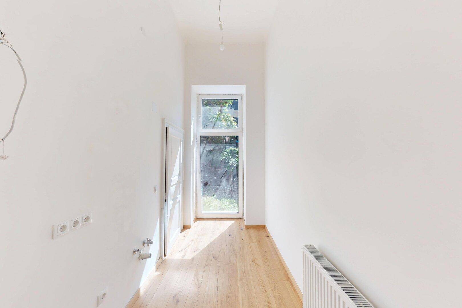 Schmaler Flur mit Holzboden und einer hohen Fenstertür, die viel Licht hereinlässt.