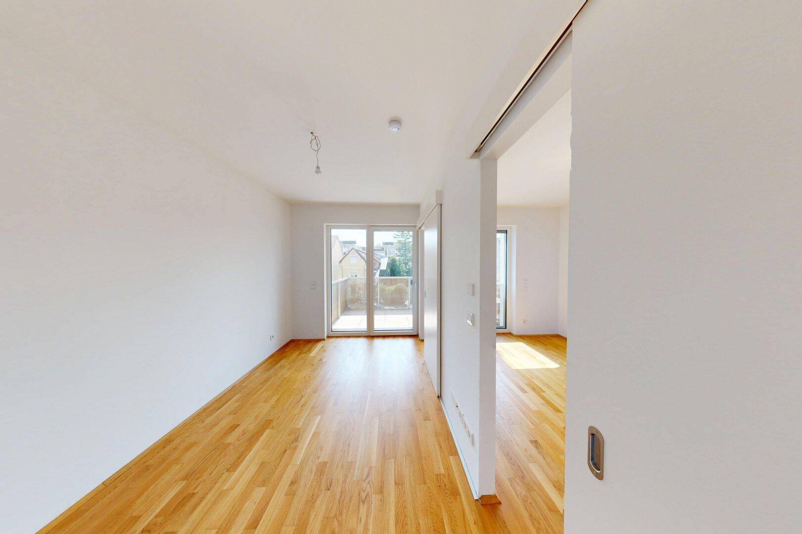 Heller Wohnraum mit Holzboden und Zugang zu einem Balkon, bietet viel natürliches Licht.