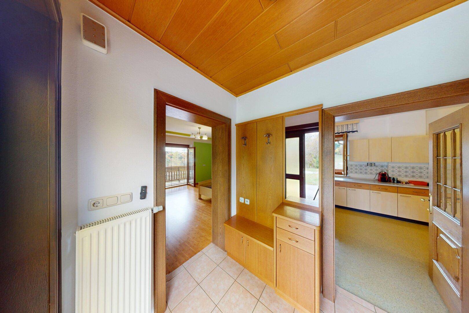 Eingangsbereich mit Holzdecke, Fliesenboden und Garderobe, Blick in Küche und Wohnzimmer.