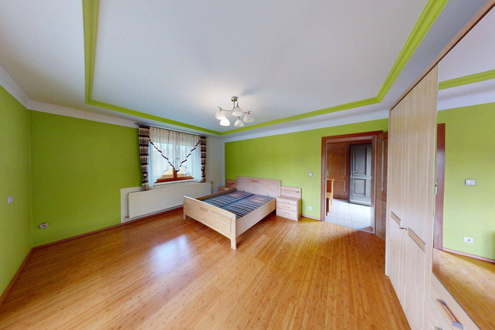 Geräumiges Schlafzimmer mit Holzboden, grünen Akzentwänden und traditionellen Möbeln.