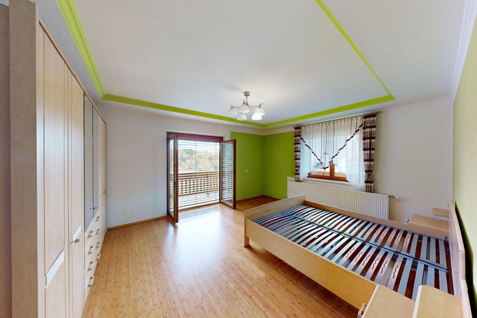 Helles Schlafzimmer mit Holzboden, grünen Wänden und Zugang zu einem Balkon.