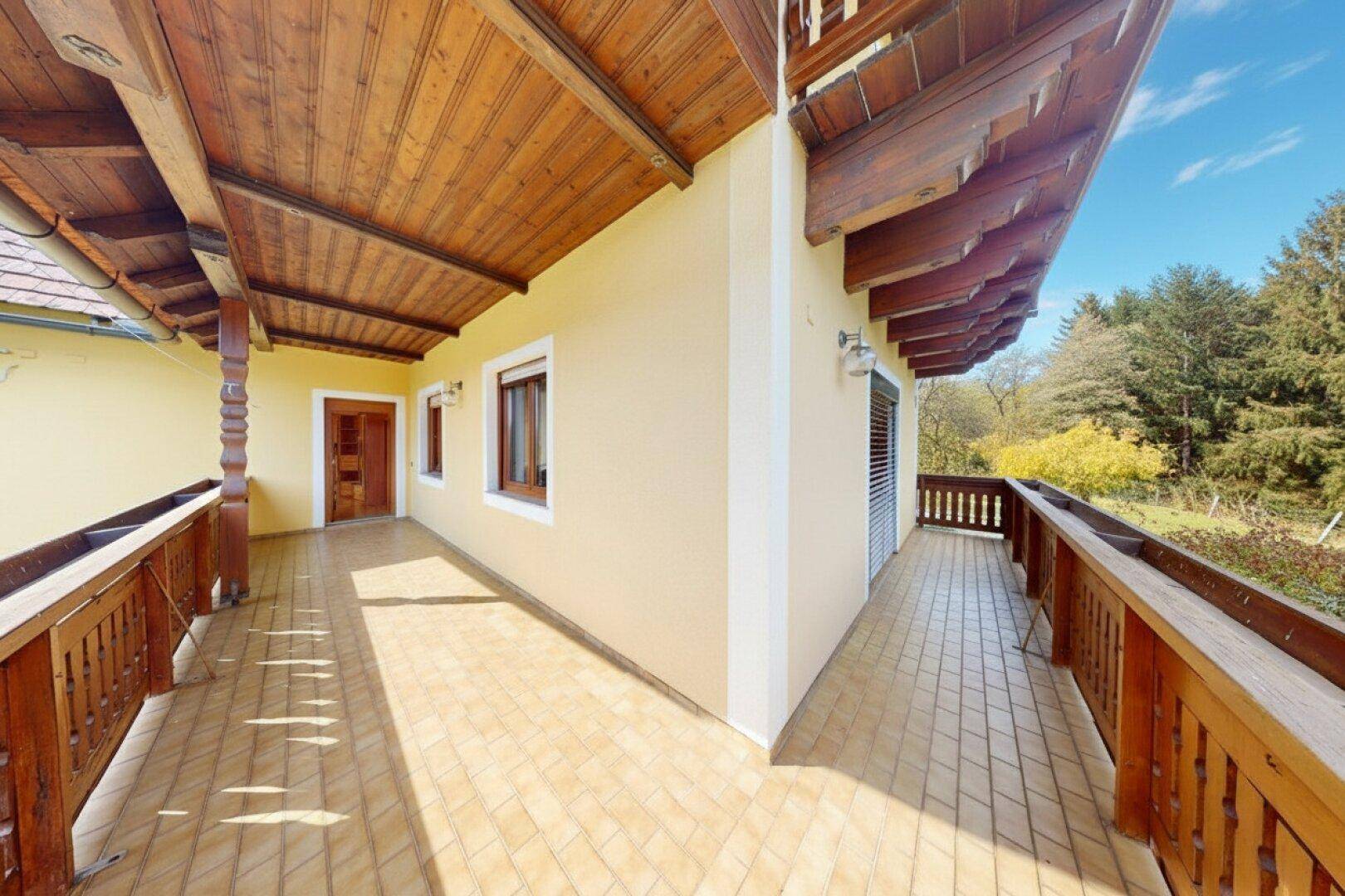 Langer überdachter Balkon mit Holzboden und Holzgeländer, ideal für Entspannung im Freien.