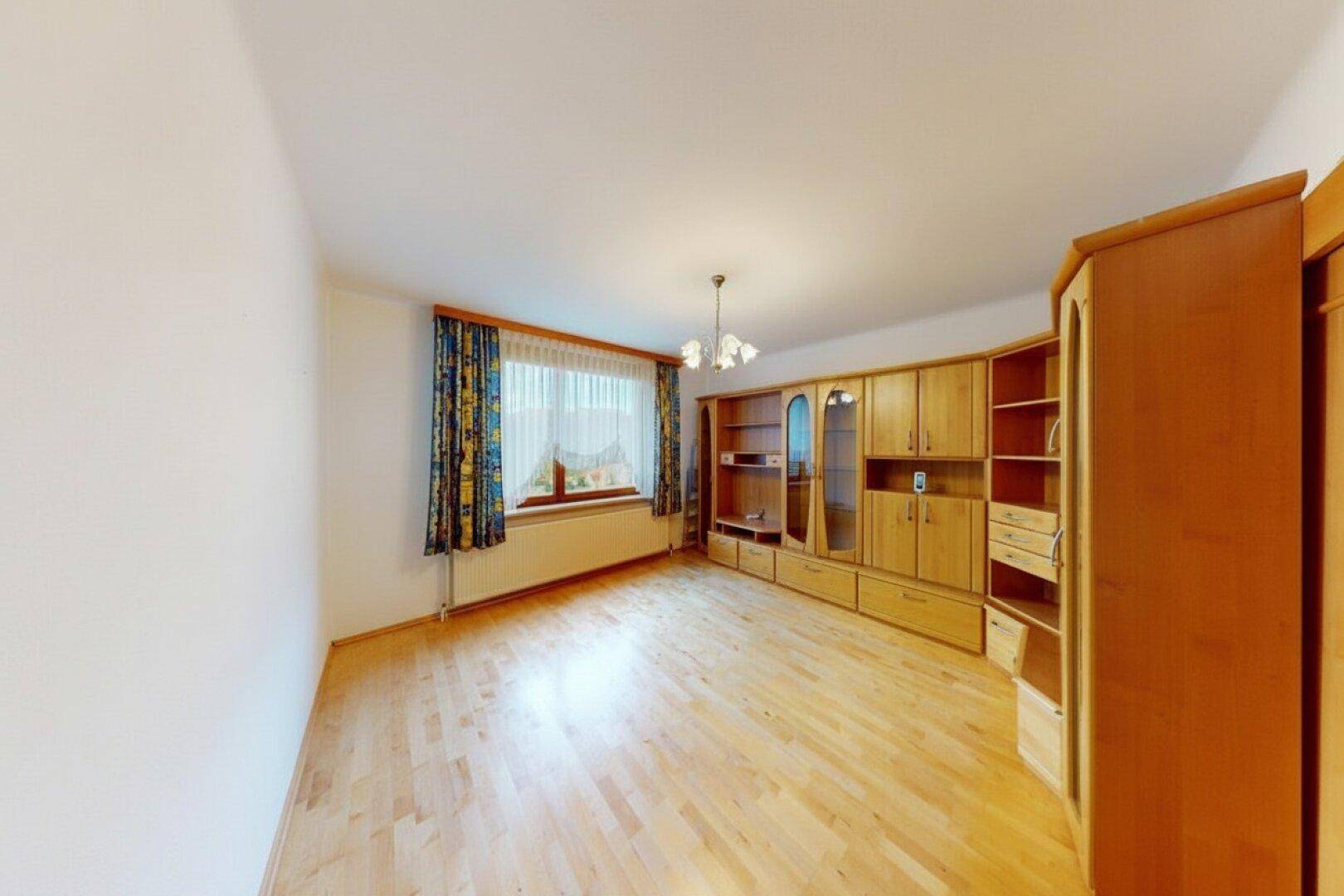 Geräumiges Wohnzimmer mit Holzboden, Fenster und traditionellem Wandschrank.