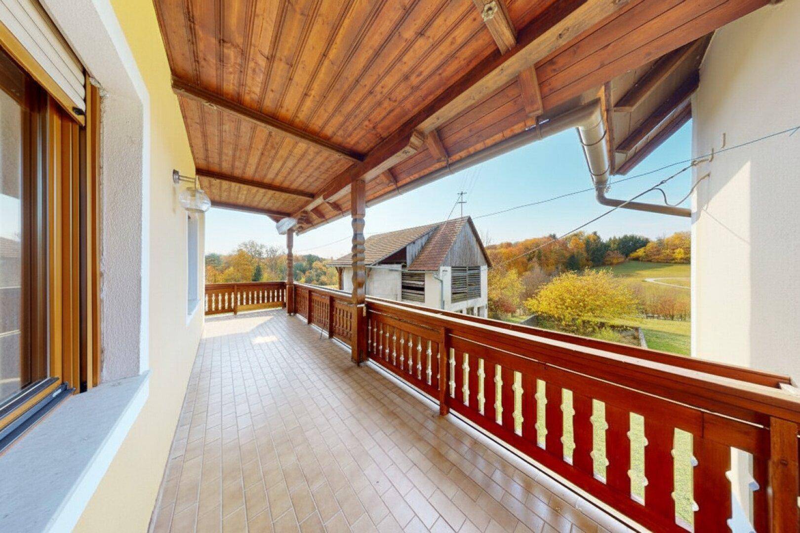 Geräumiger Balkon mit Holzdach und Fliesenboden, umgeben von ländlicher Natur.
