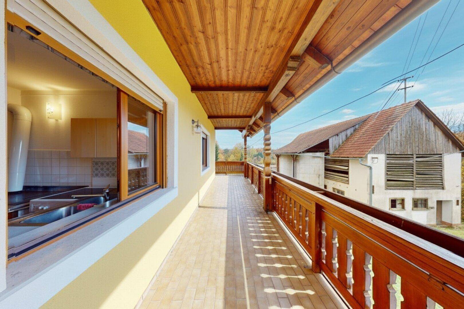 Überdachter Balkon mit Fliesenboden und Holzbalken, bietet Blick auf die Umgebung.