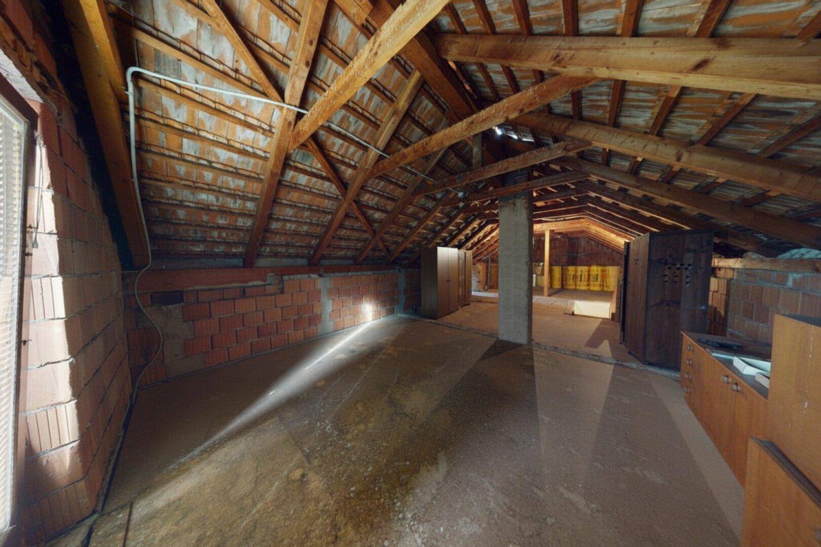 Unausgebauter Dachboden mit sichtbaren Holzbalken und Ziegelwänden, bietet Ausbaupotenzial.