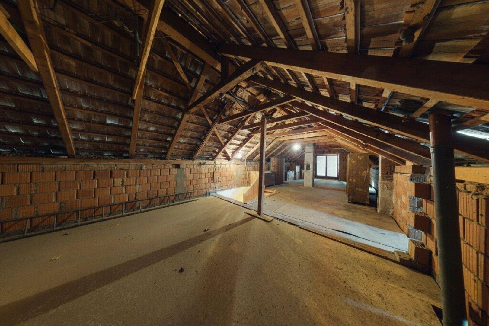 Großer unausgebauter Dachboden mit Holzdachstuhl und Ziegelwänden, ideal für zukünftige Projekte.