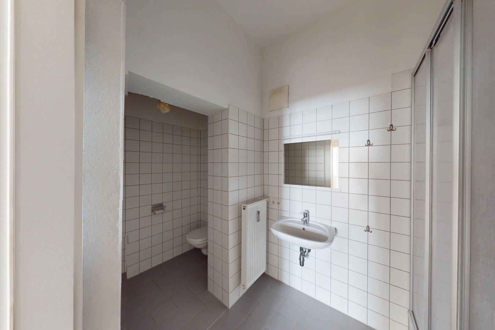 Gefliestes Badezimmer mit Dusche, Waschbecken und Toilette in einem separaten Bereich.
