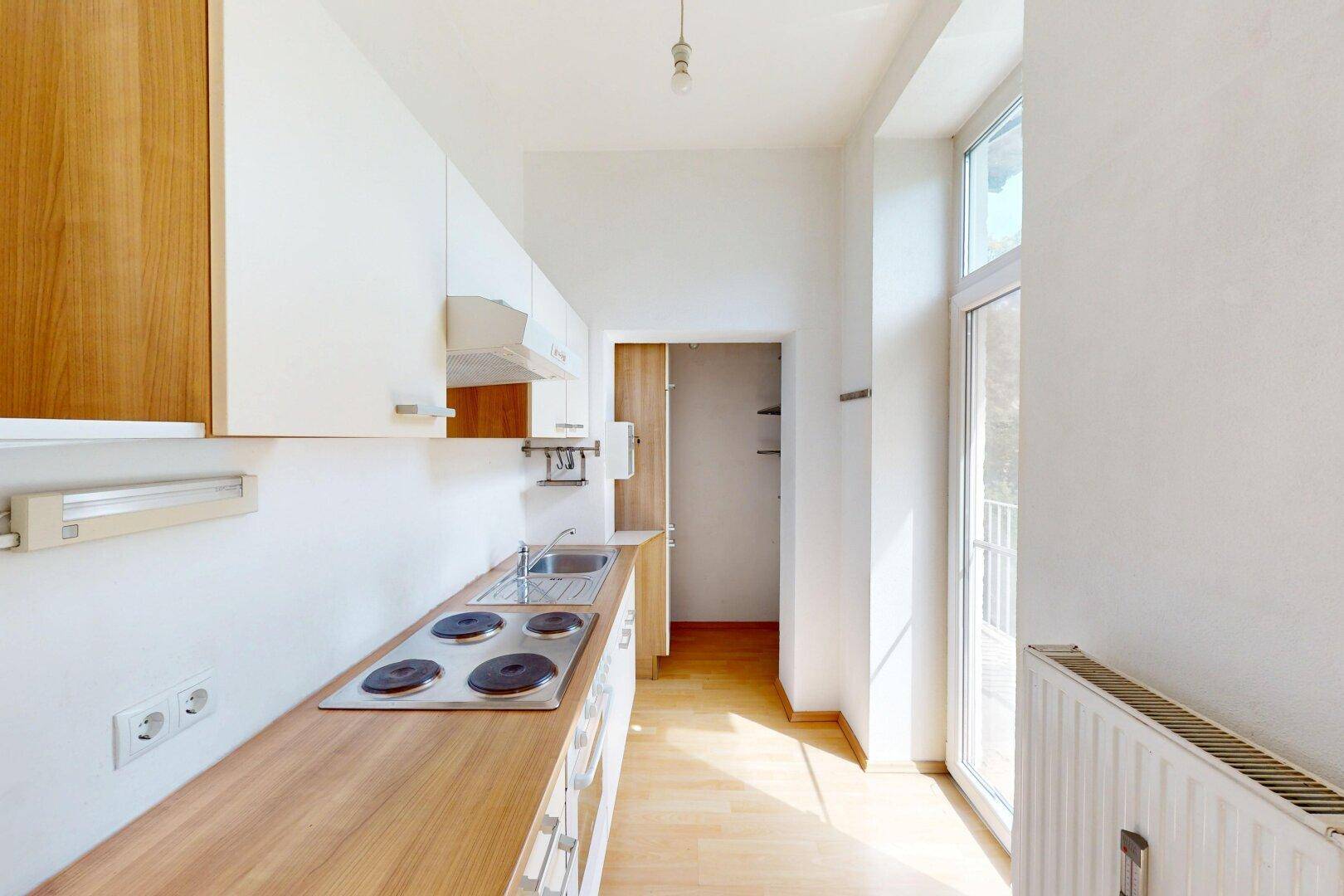 Schmale Küche mit Holz-Arbeitsplatte, Einbauschränken und Zugang zu einem kleinen Balkon.