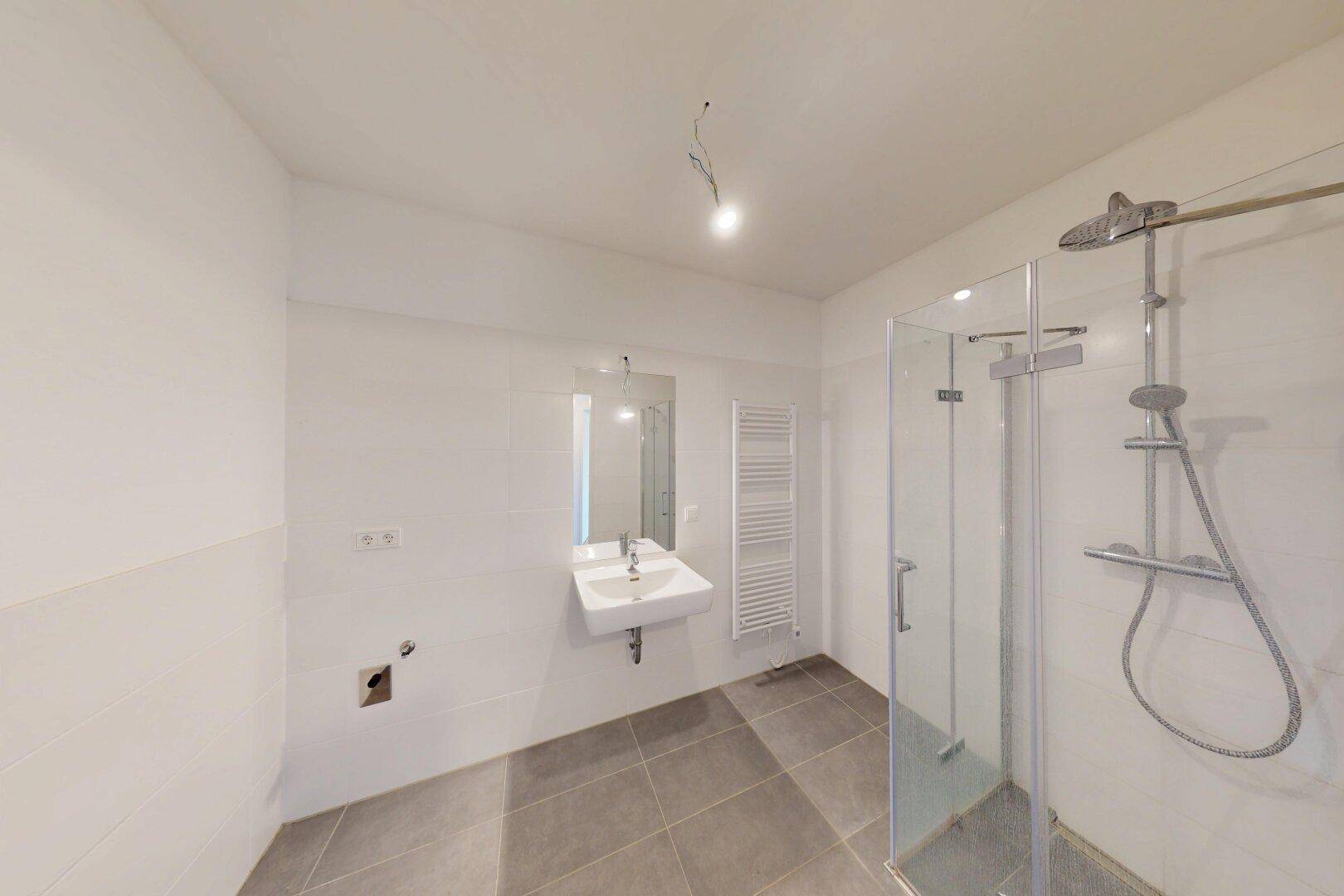 Modernes Badezimmer mit weißen Wandfliesen, grauen Bodenfliesen und einer Glasdusche.