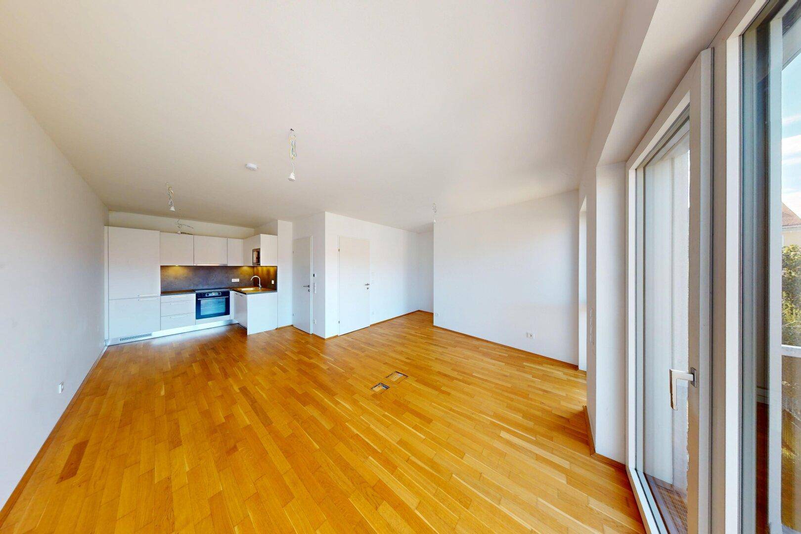 Heller, offener Wohnbereich mit integrierter Küche und Zugang zum Balkon, ausgestattet mit Parkettboden.