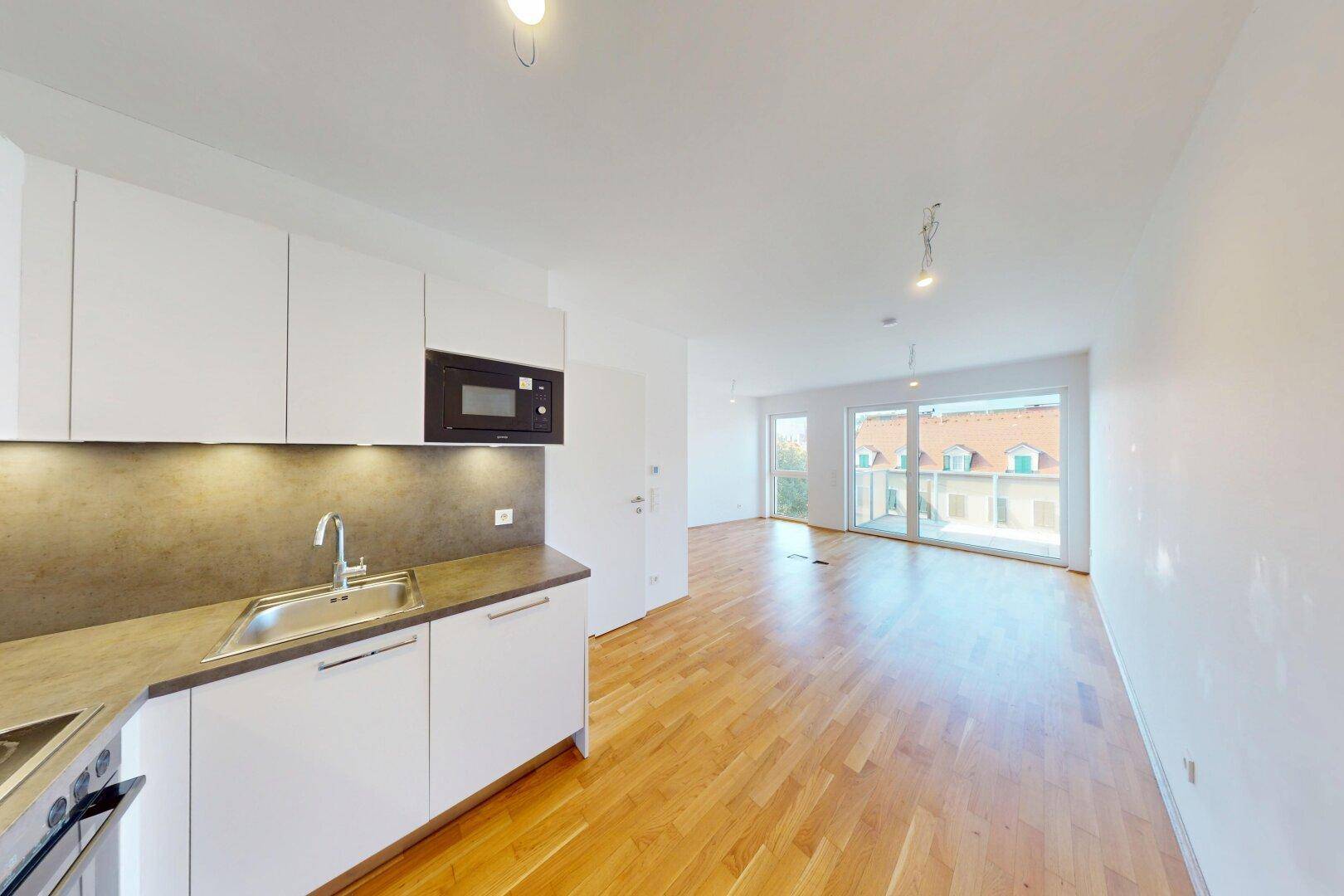 Moderne, offene Küche mit weißen Schränken, integrierter Mikrowelle und Blick in den Wohnbereich.