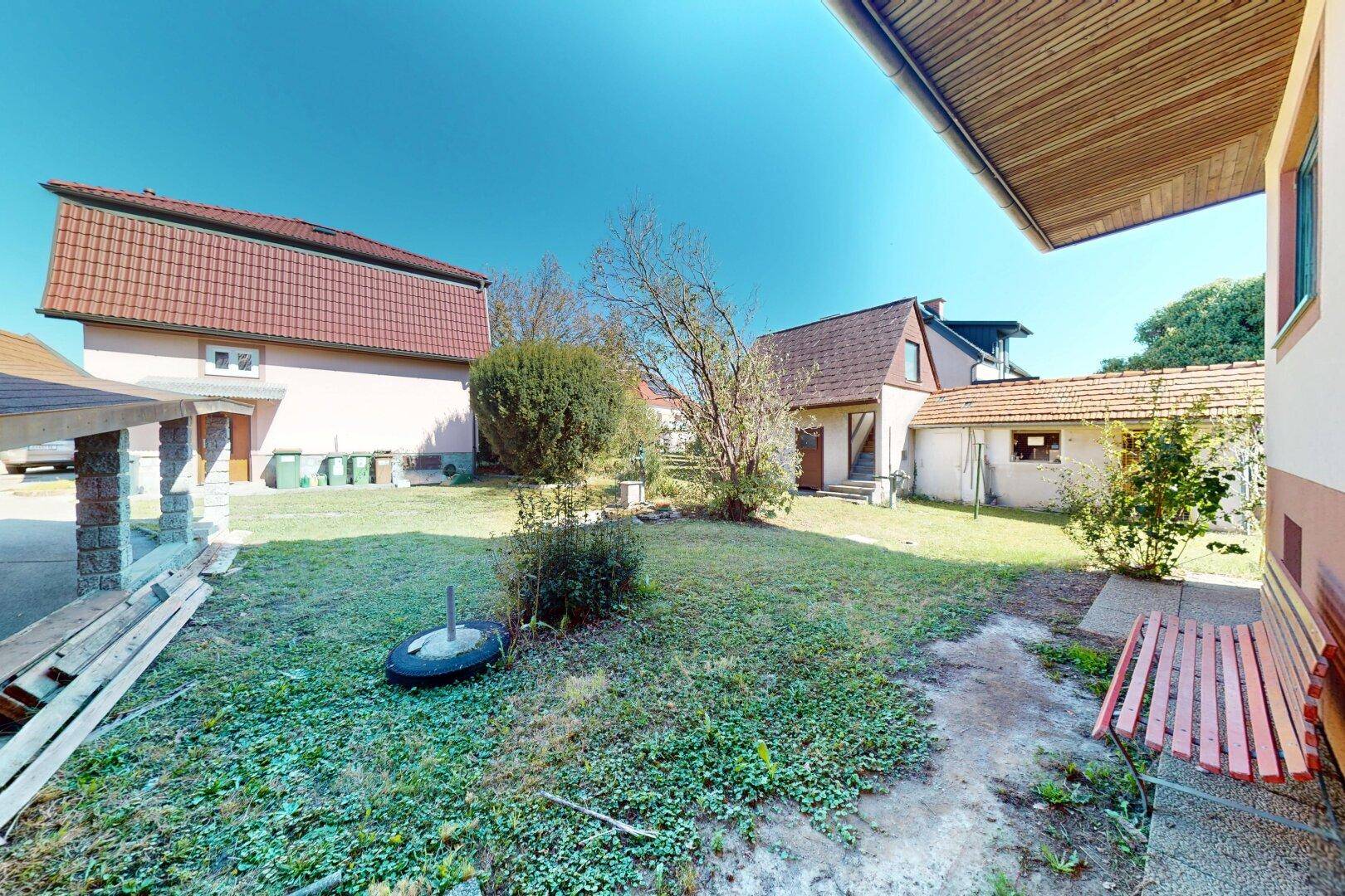 Blick in den hinteren Gartenbereich zwischen den Gebäuden mit Rasenfläche und Sitzbank.