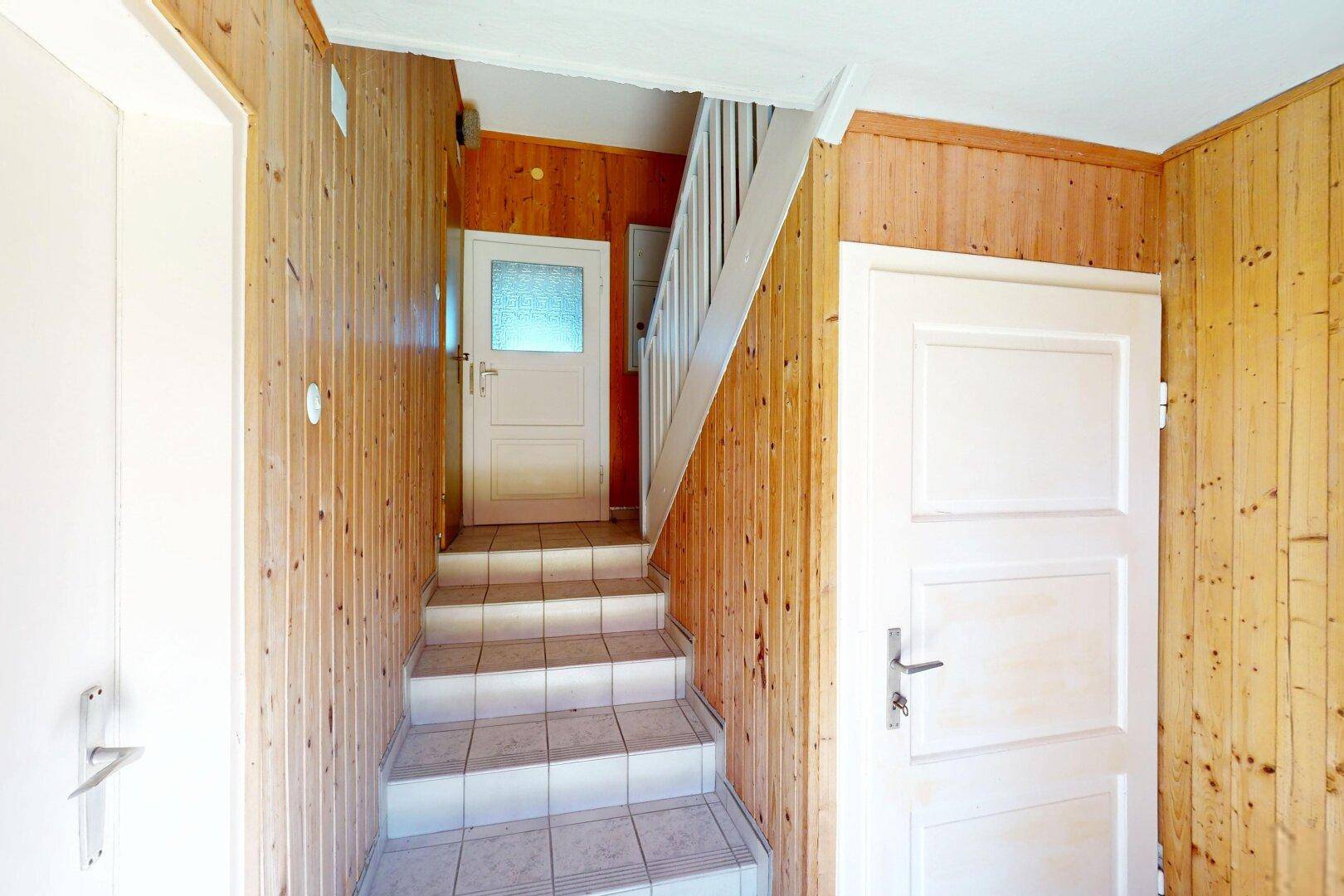 Heller Flur mit Holzvertäfelung, weiß gefliestem Boden und Treppenaufgang.