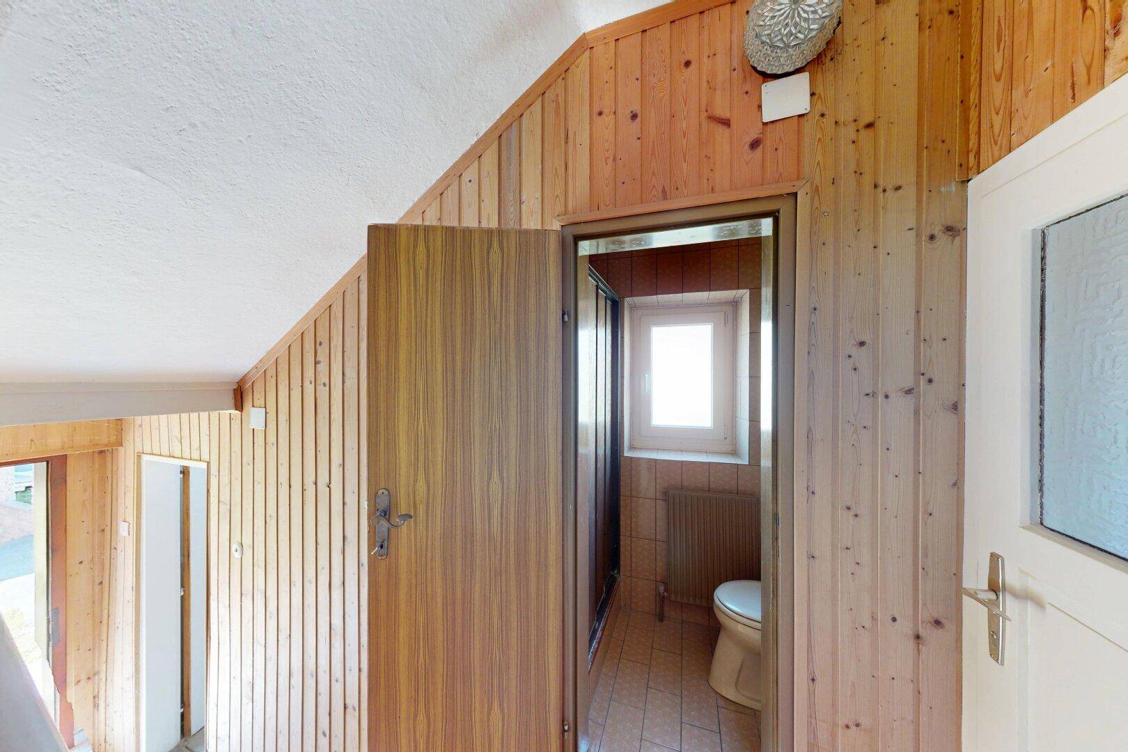 Flur mit Holzvertäfelung und Zugang zu einem kleinen WC mit Fenster.