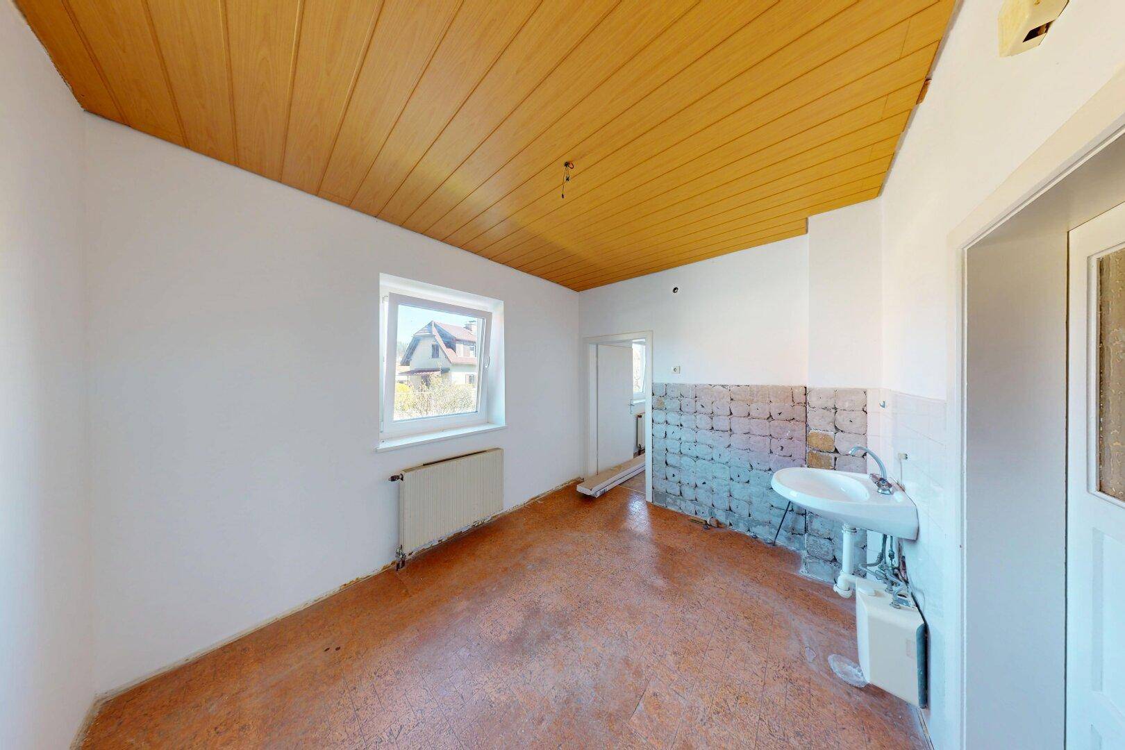 Leerer Raum mit gelber Holzdecke, Fenster und Heizkörper, bereit für eine neue Kücheninstallation.