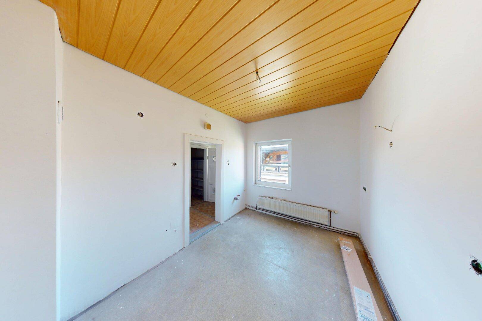 Leerer Raum mit gelber Holzdecke, Fenster und Heizkörper, bereit für die weitere Gestaltung.