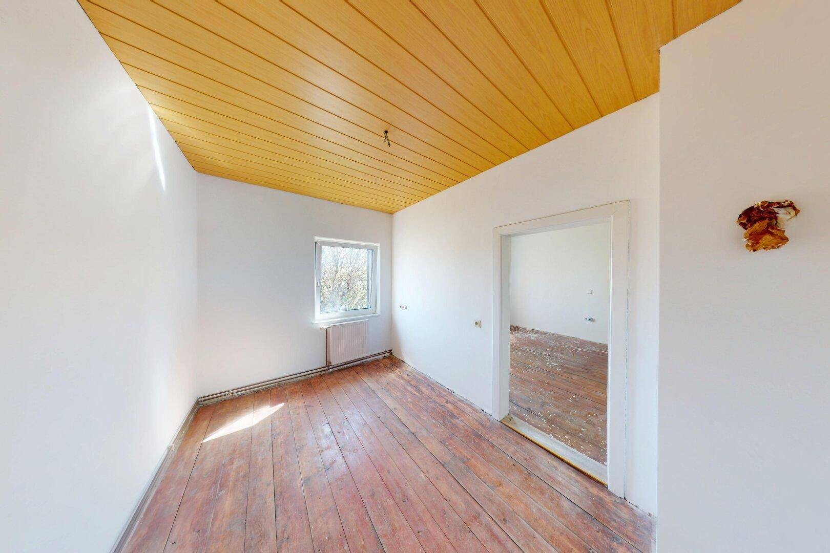 Leerer Raum mit gelber Holzdecke, Fenster und altem Holzdielenboden, bereit zur Renovierung.
