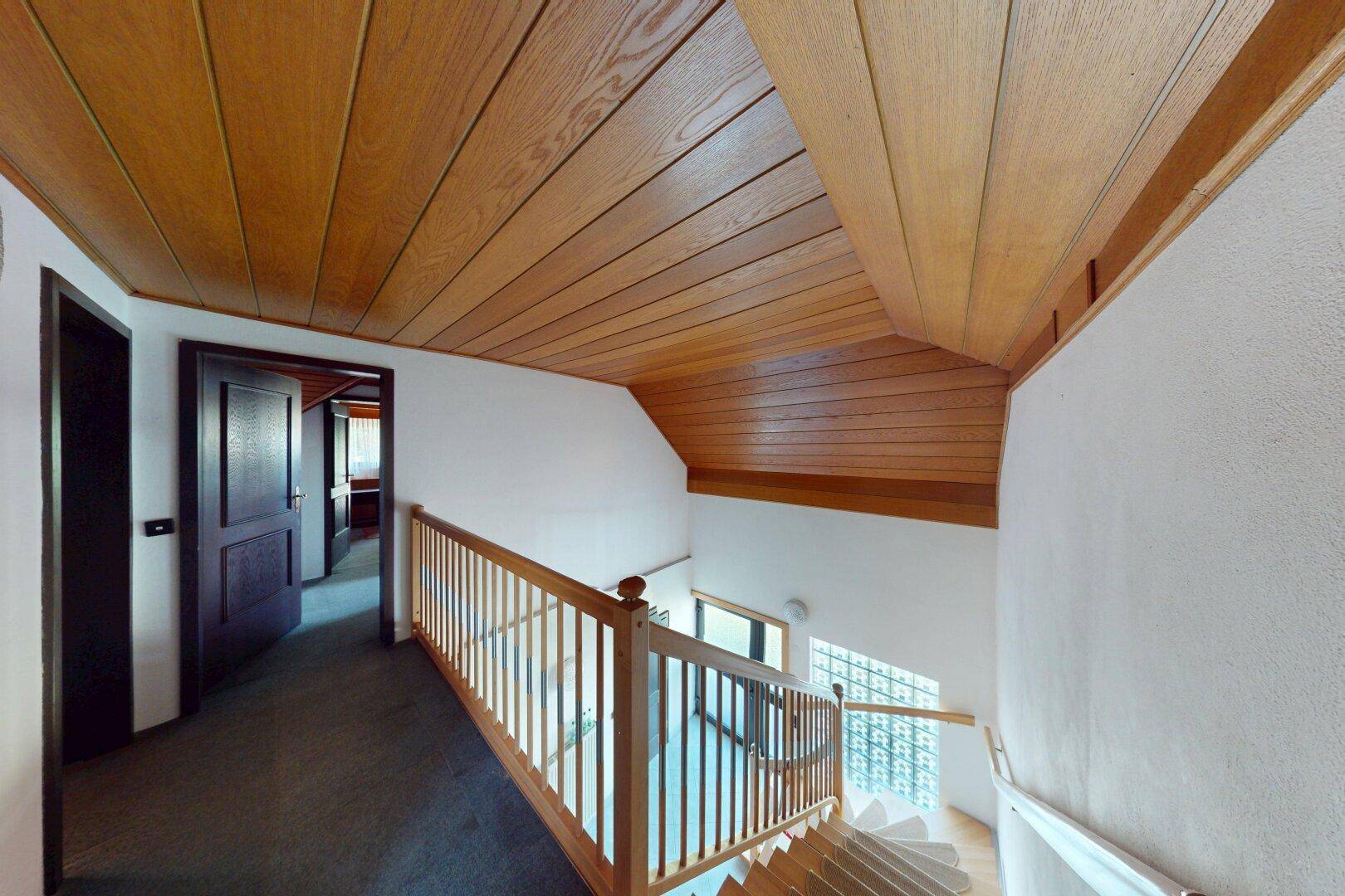 Oberer Flur mit Holzdecke, Teppichboden und Blick auf die untere Etage.