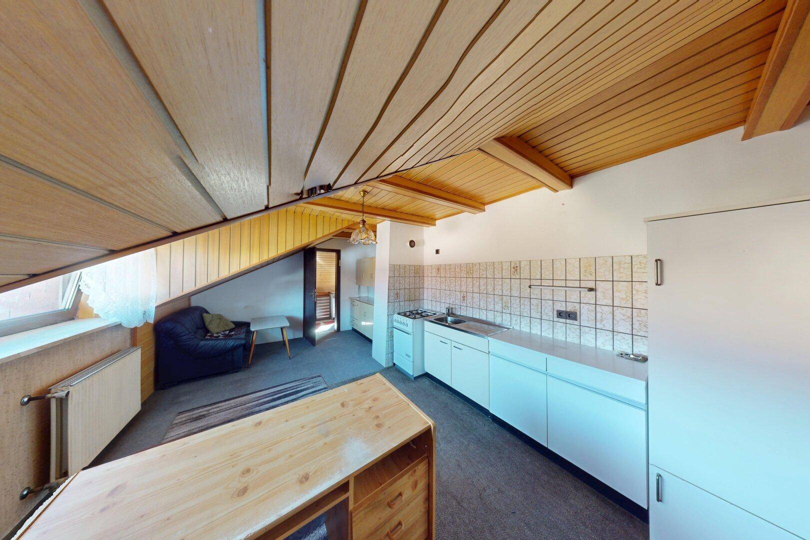 Dachbodenraum mit kleiner Küchenzeile, schrägen Holzdecken und Fenster.