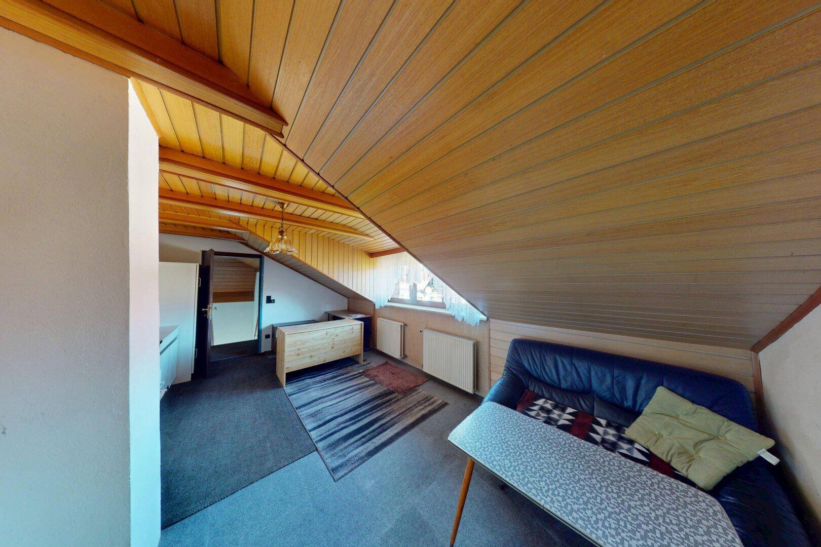 Gemütlicher Dachbodenraum mit schrägen Holzdecken, Sofa und Teppich.