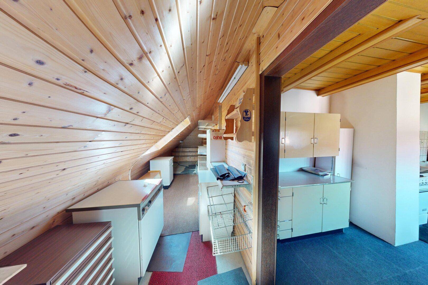 Dachbodenbereich mit Holzverkleidung, kleiner Küchenzeile und Stauraum.