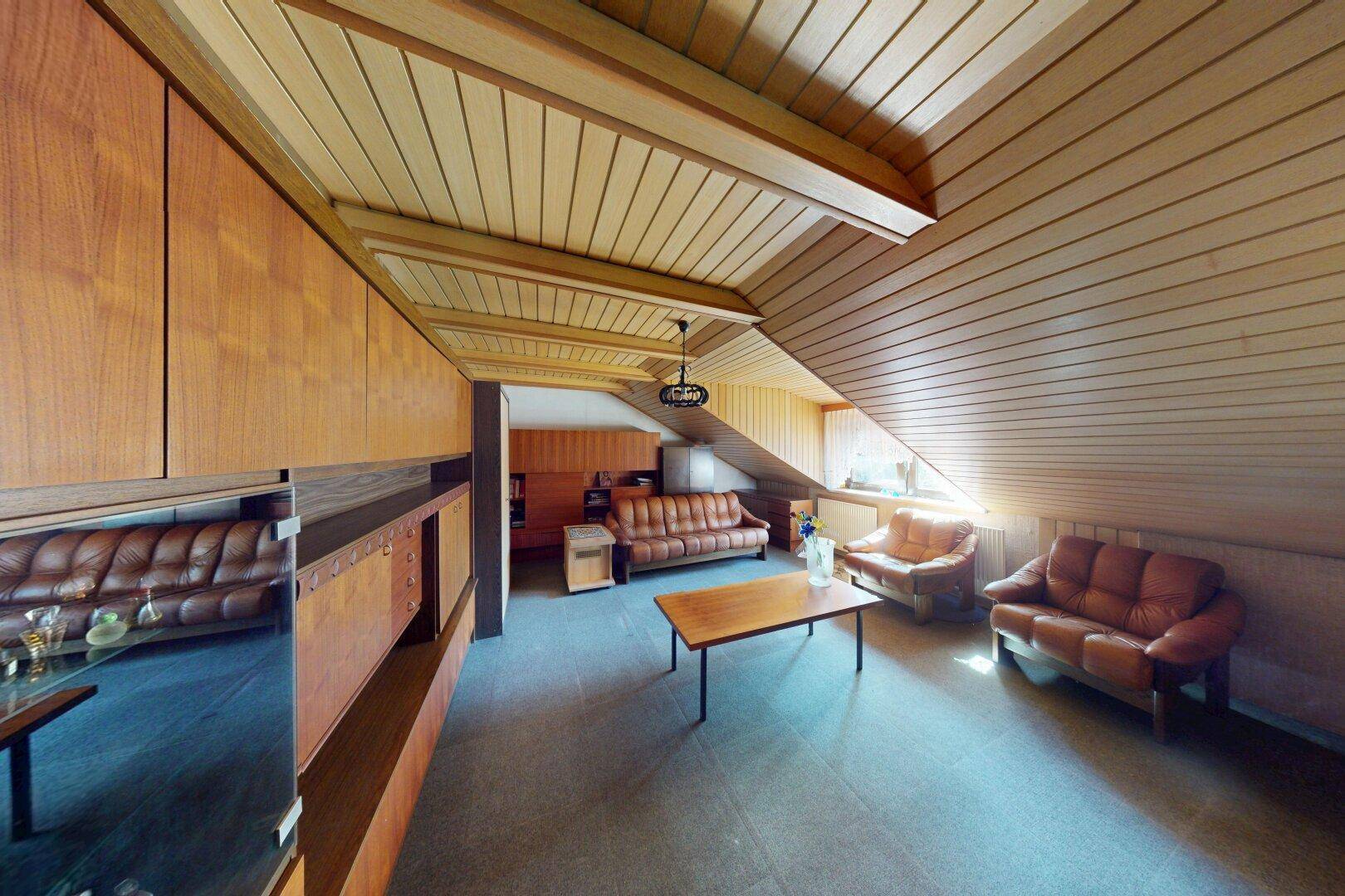 Geräumiges Wohnzimmer im Dachgeschoss mit viel Holz, Ledermöbeln und integrierten Schränken.