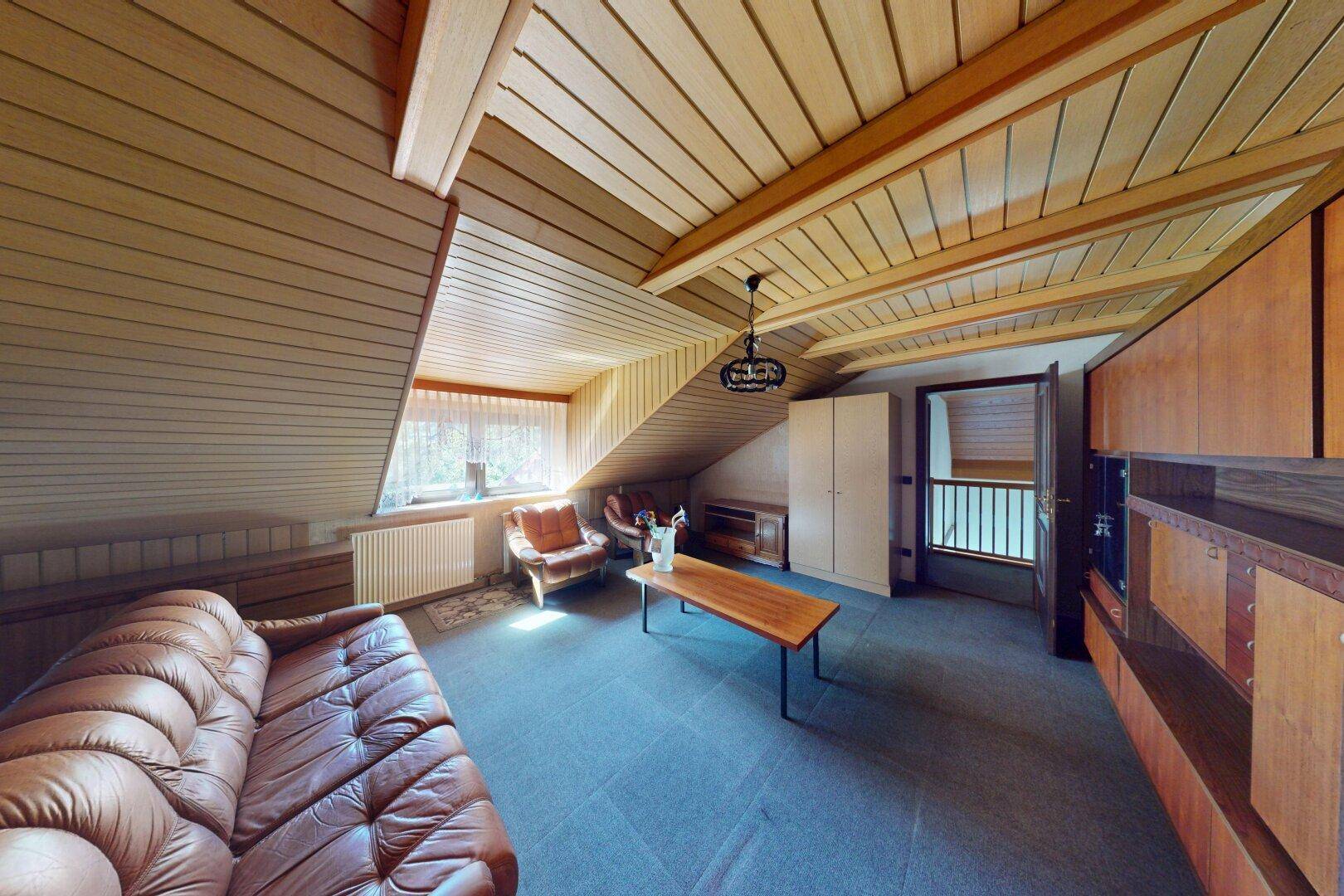 Gemütliches Wohnzimmer im Dachgeschoss mit Holzverkleidung, Ledersofa und schrägen Decken.