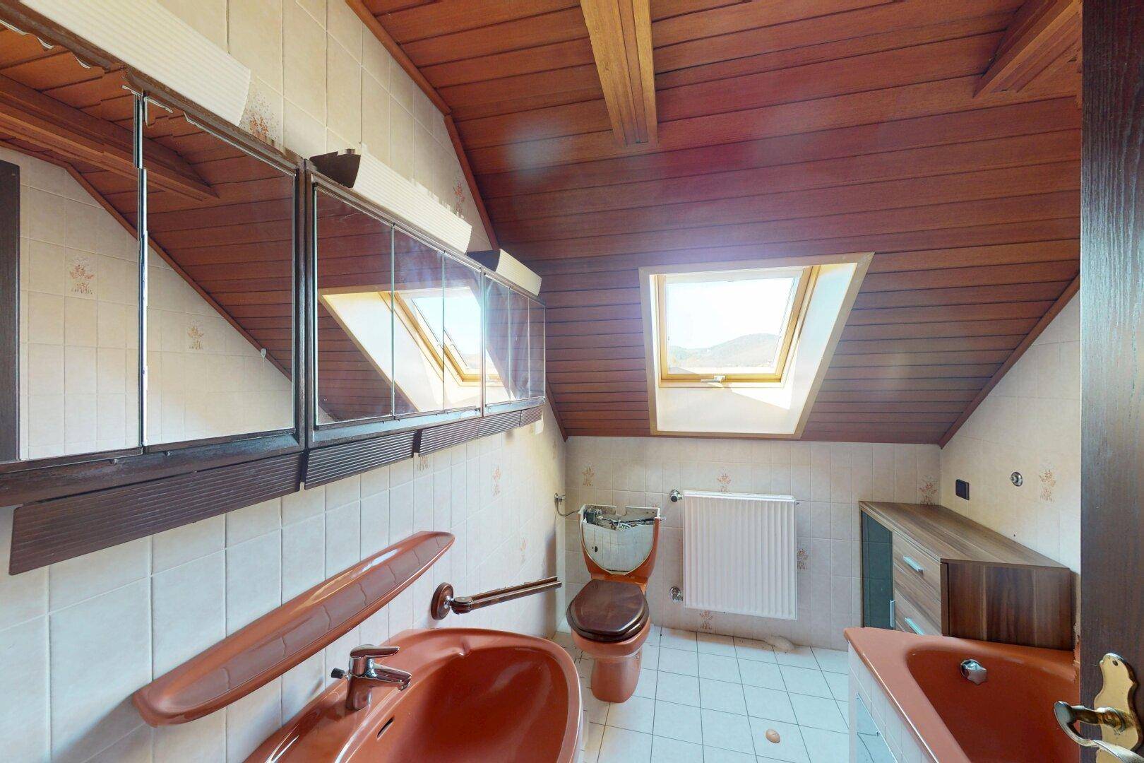 Badezimmer im Dachgeschoss mit schrägen Decken, orangefarbenen Armaturen und zwei Dachfenstern.