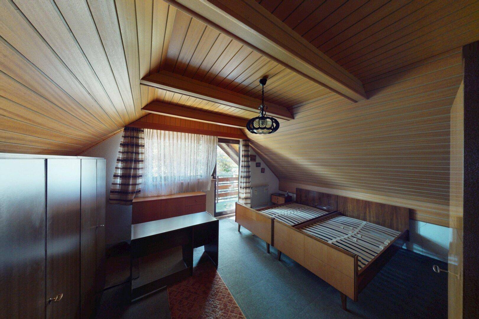 Schlafzimmer im Dachgeschoss mit Holzverkleidung, zwei Einzelbetten und Zugang zu einem Balkon.