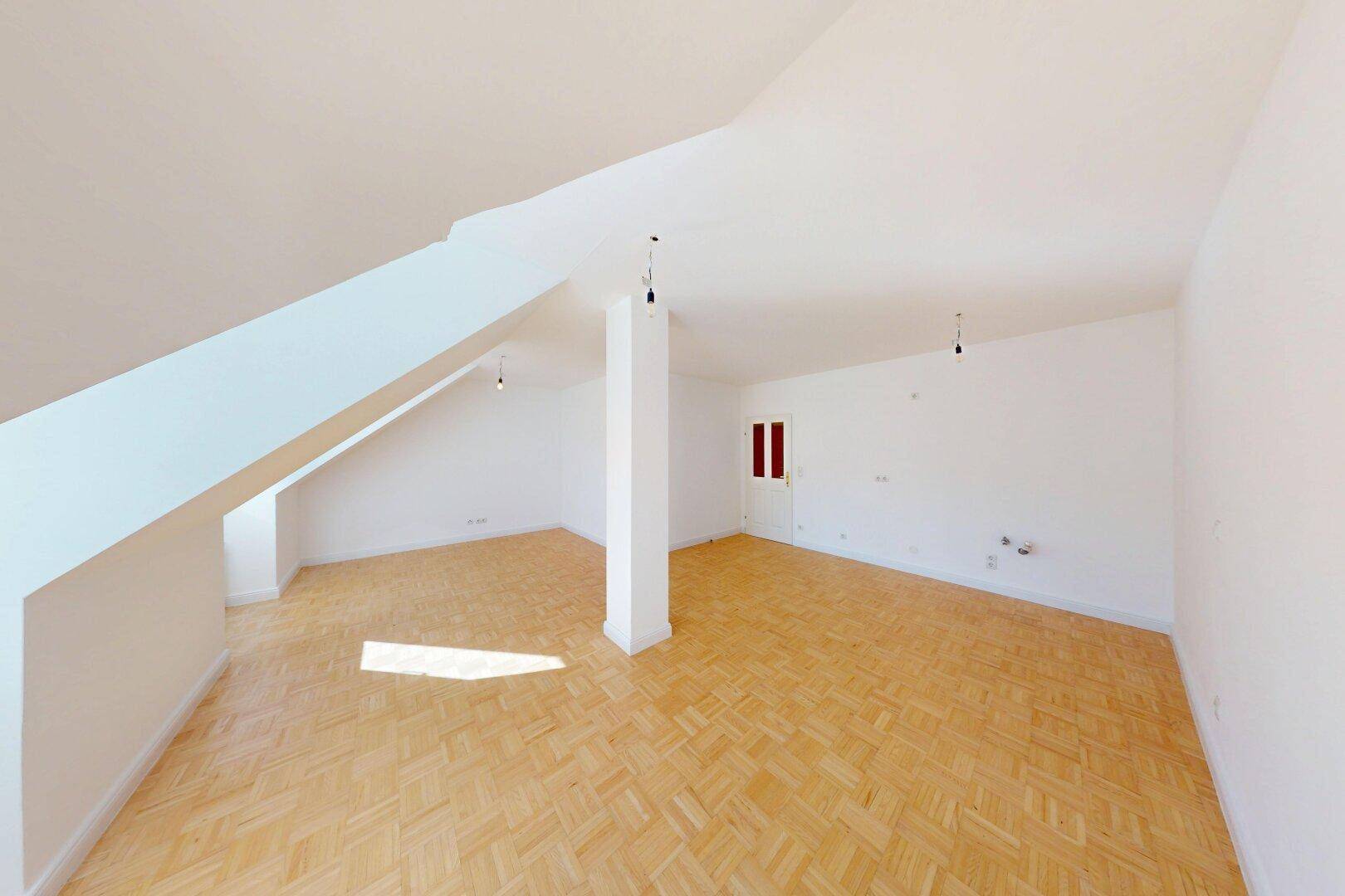 Geräumiger Dachgeschossraum mit Parkettboden, weiß gestrichenen Wänden und sichtbaren Dachschrägen.