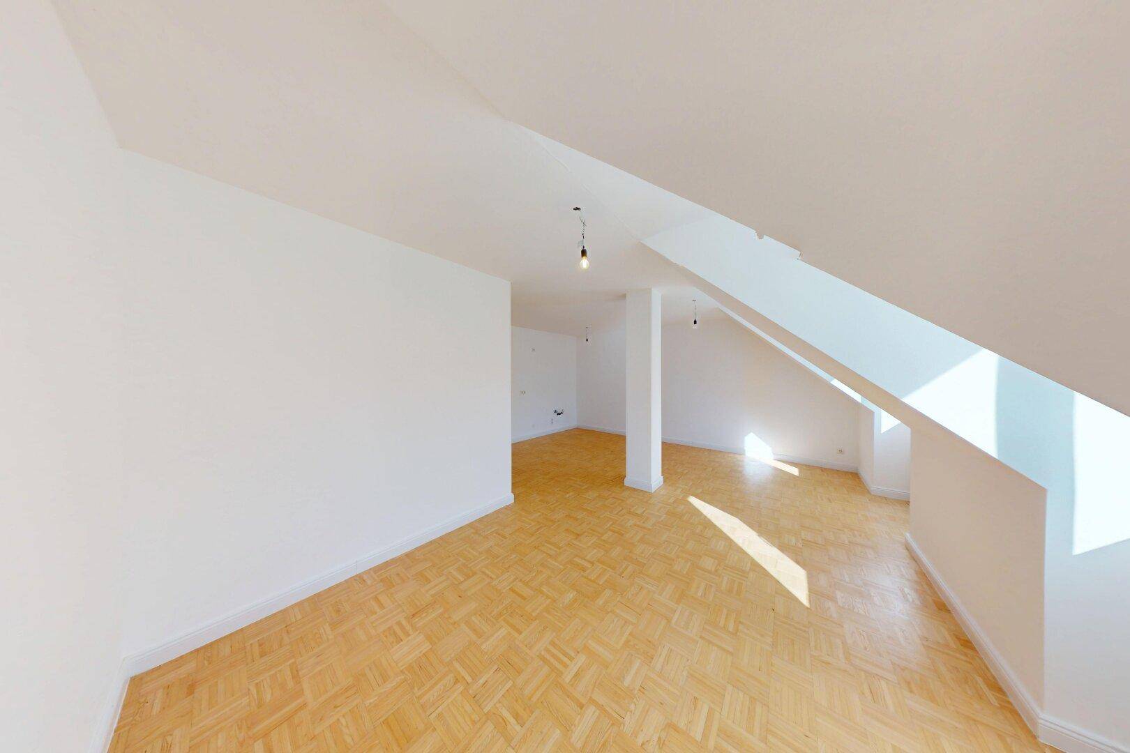 Heller Wohnbereich im Dachgeschoss mit Parkettboden und schrägen Wänden, bietet viel Tageslicht.