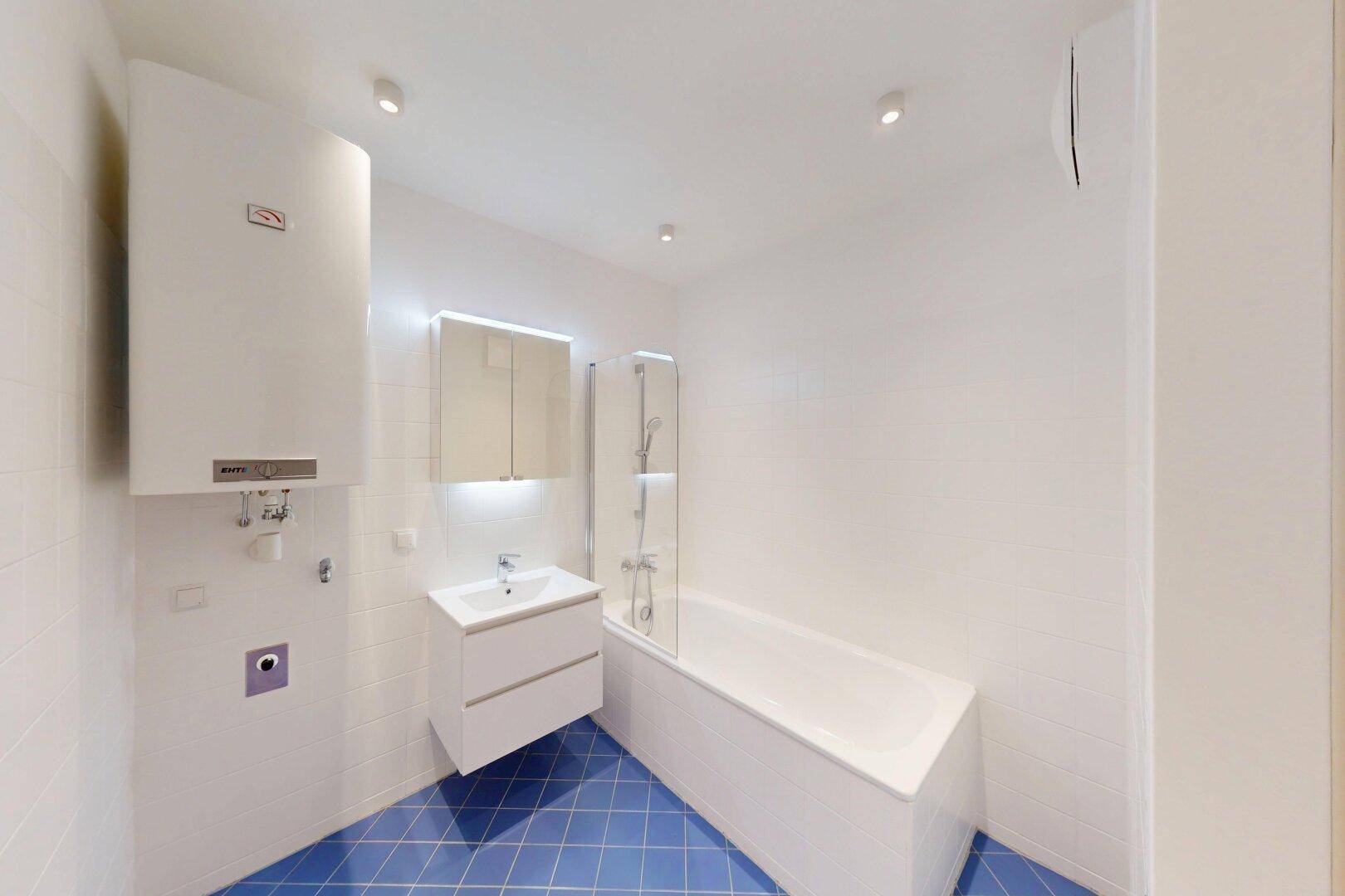 Modernes Badezimmer mit blauen Fliesen, Badewanne mit Duschfunktion und Waschbecken.
