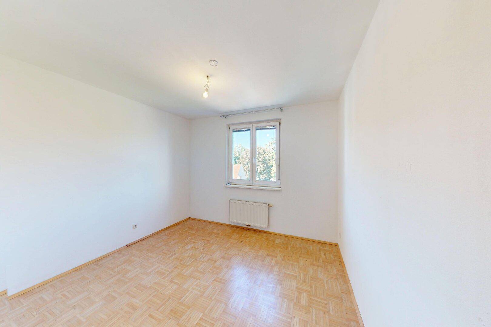 Geräumiges Schlafzimmer mit Parkettboden und Fenster, das viel Tageslicht hereinlässt.