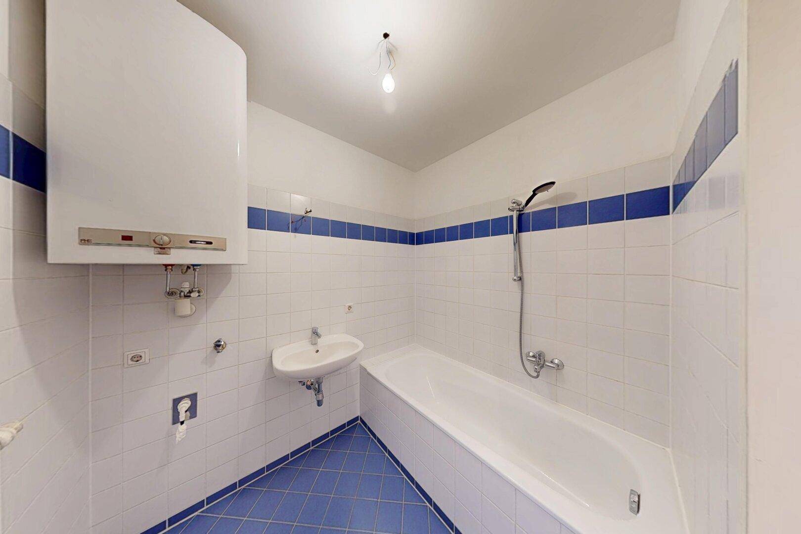 Funktionales Badezimmer mit Badewanne, Waschbecken und blau-weißen Fliesen, inklusive Warmwasserboiler.