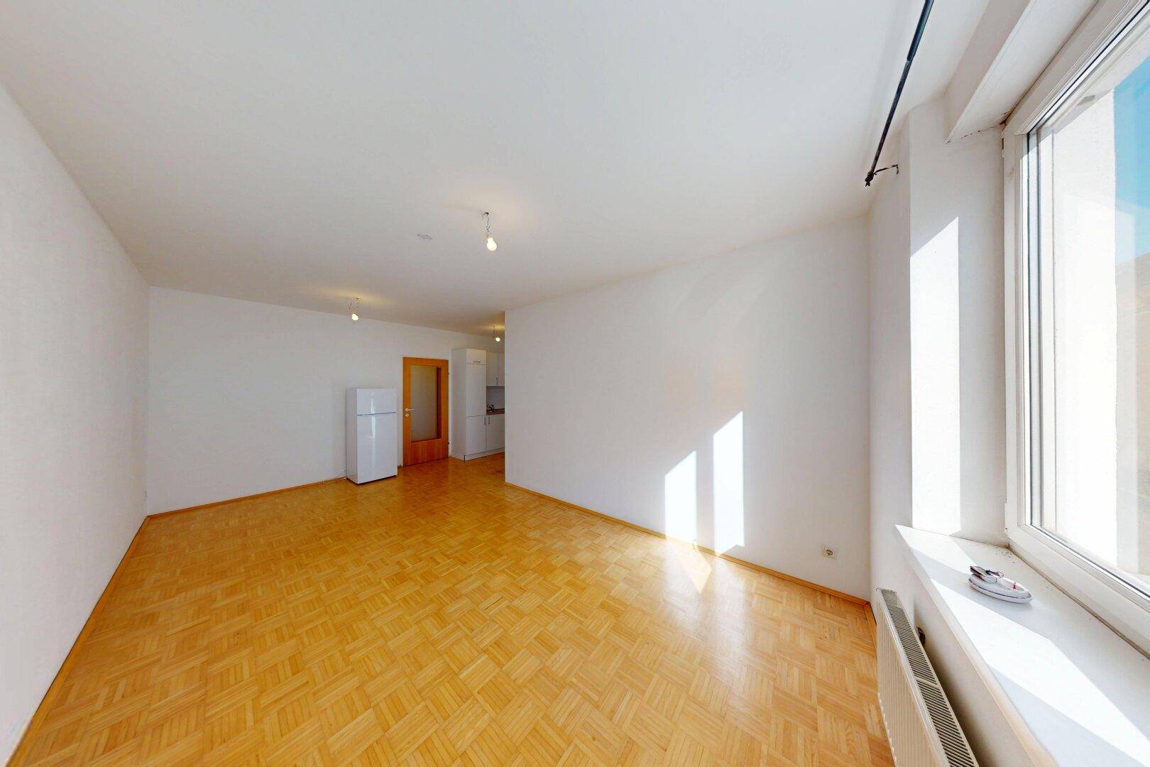 Lichtdurchflutetes Wohnzimmer mit Parkettboden und großem Fenster, das eine angenehme Atmosphäre schafft.