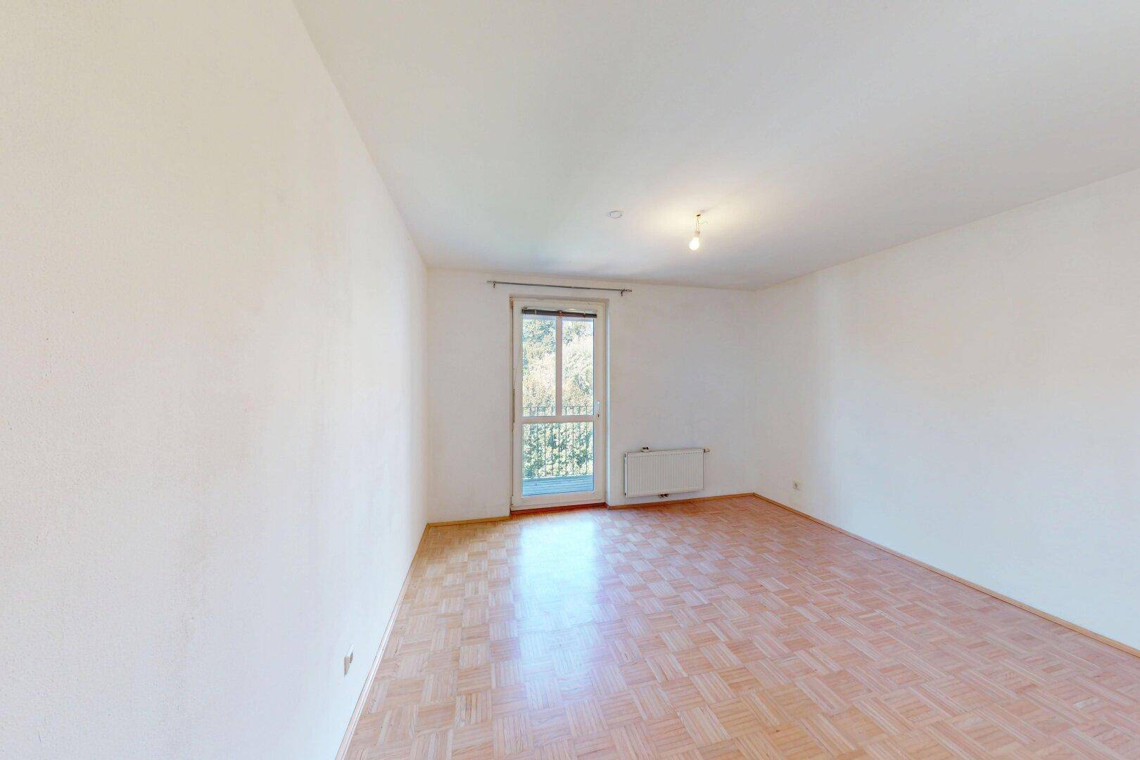 Helles Zimmer mit Parkettboden und Zugang zum Balkon, ideal für ein Schlaf- oder Arbeitszimmer.