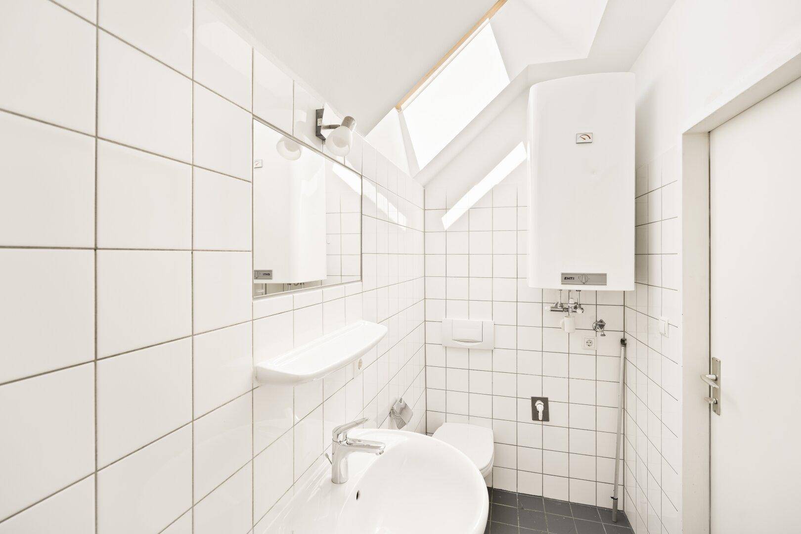 Modern gefliestes Badezimmer mit Dusche, WC und Dachfenster.