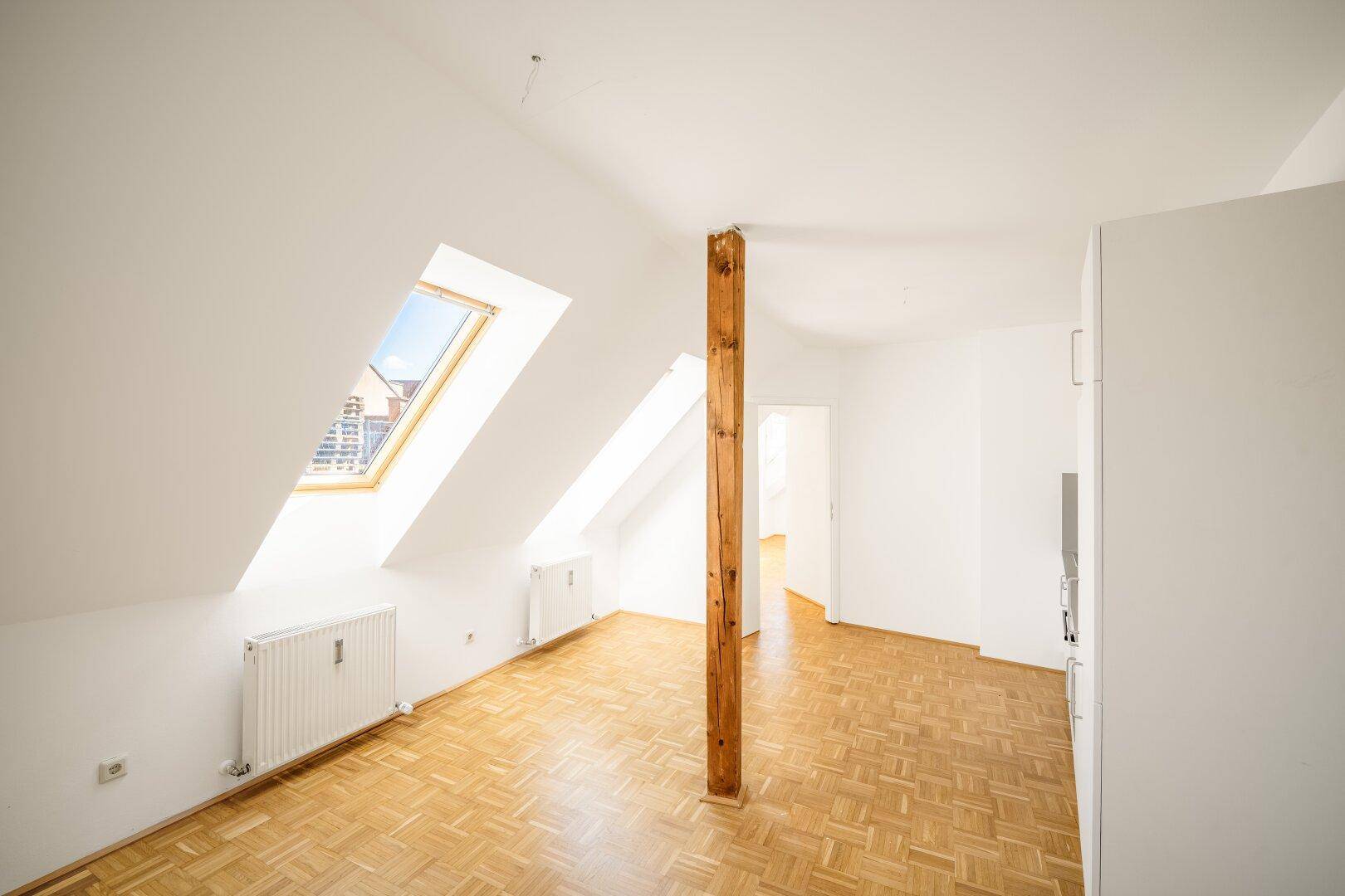 Lichtdurchflutetes Dachgeschosszimmer mit Parkettboden und schrägen Wänden.