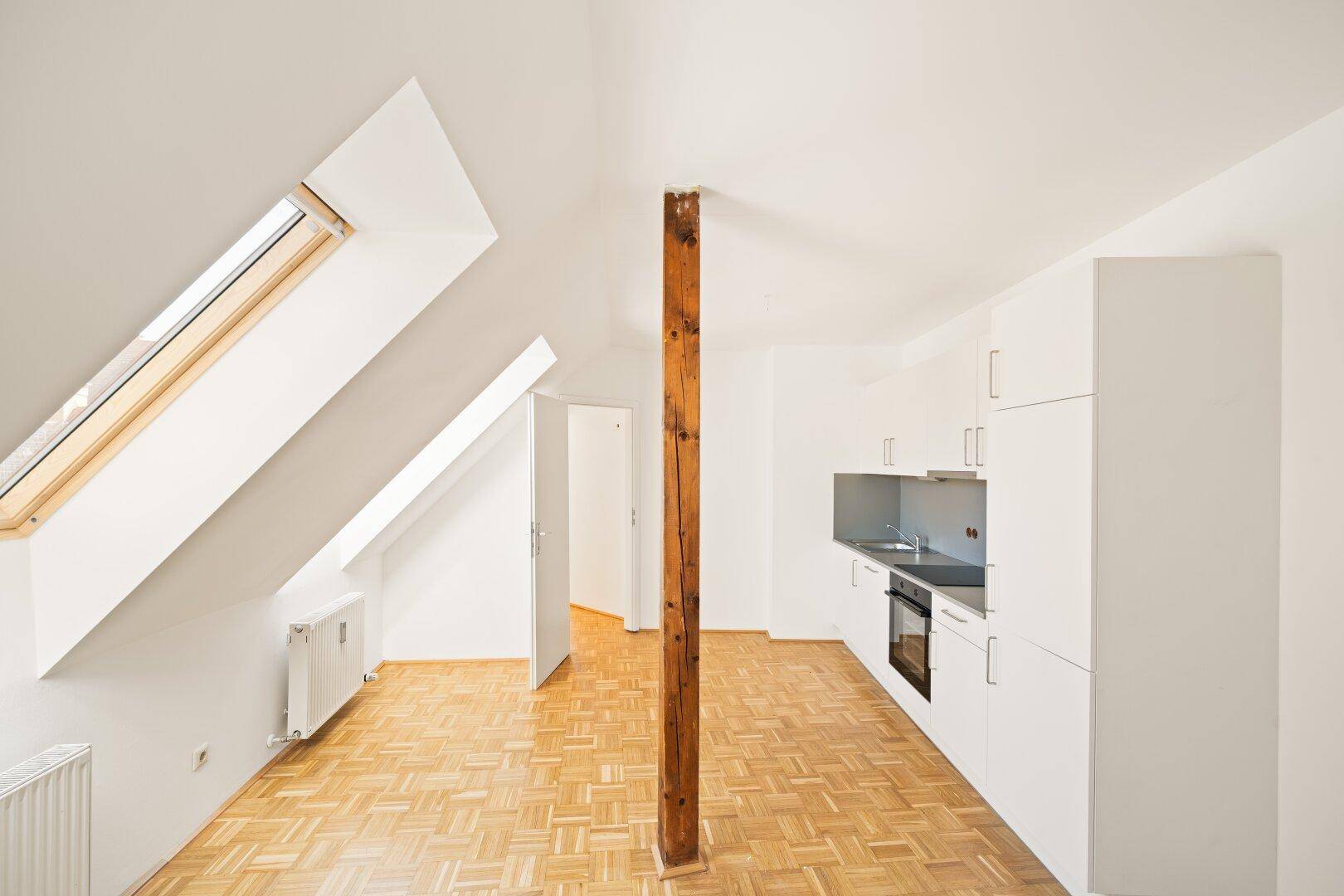 Helles Dachgeschosszimmer mit kleiner Einbauküche, Parkettboden und Dachfenstern.