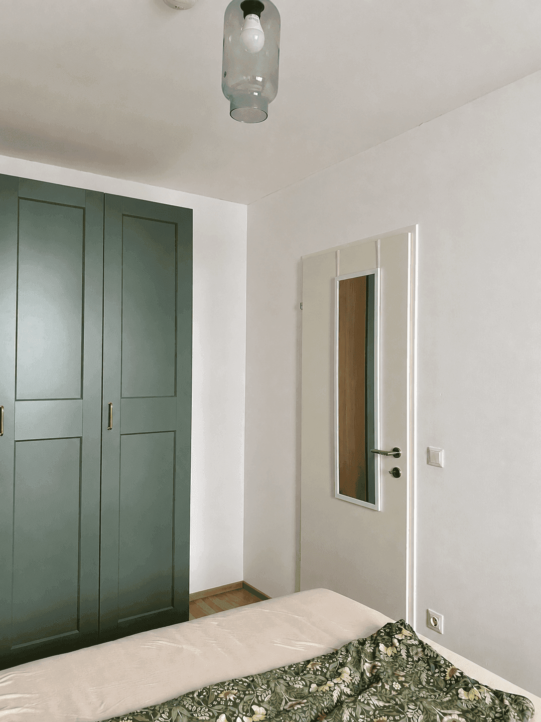 Schlafzimmer mit einem großen Kleiderschrank in dunklem Grün und hellem Holzboden.