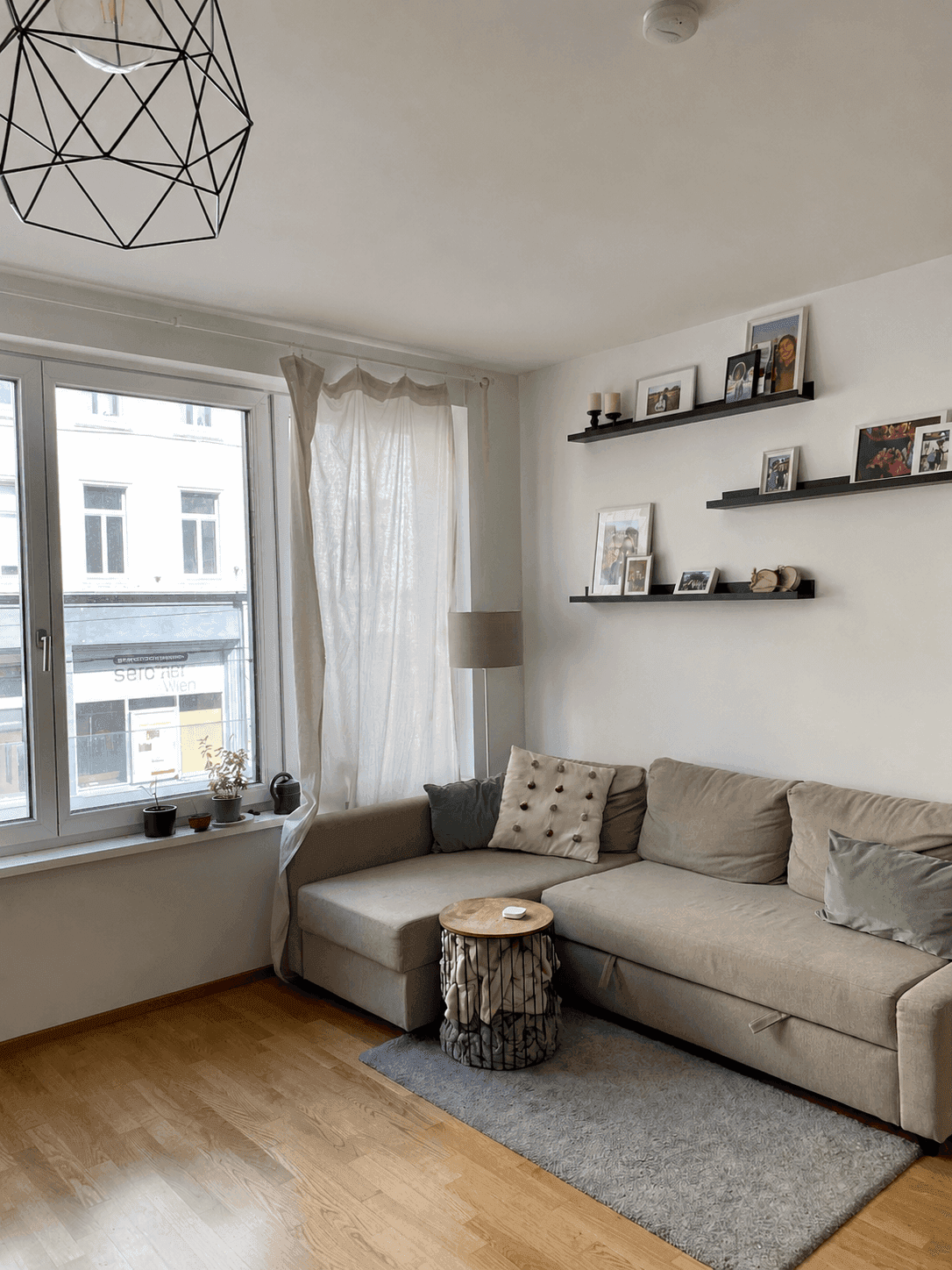 Gemütliches Wohnzimmer mit großem Ecksofa, Holzboden und Blick auf die Stadtstraße.