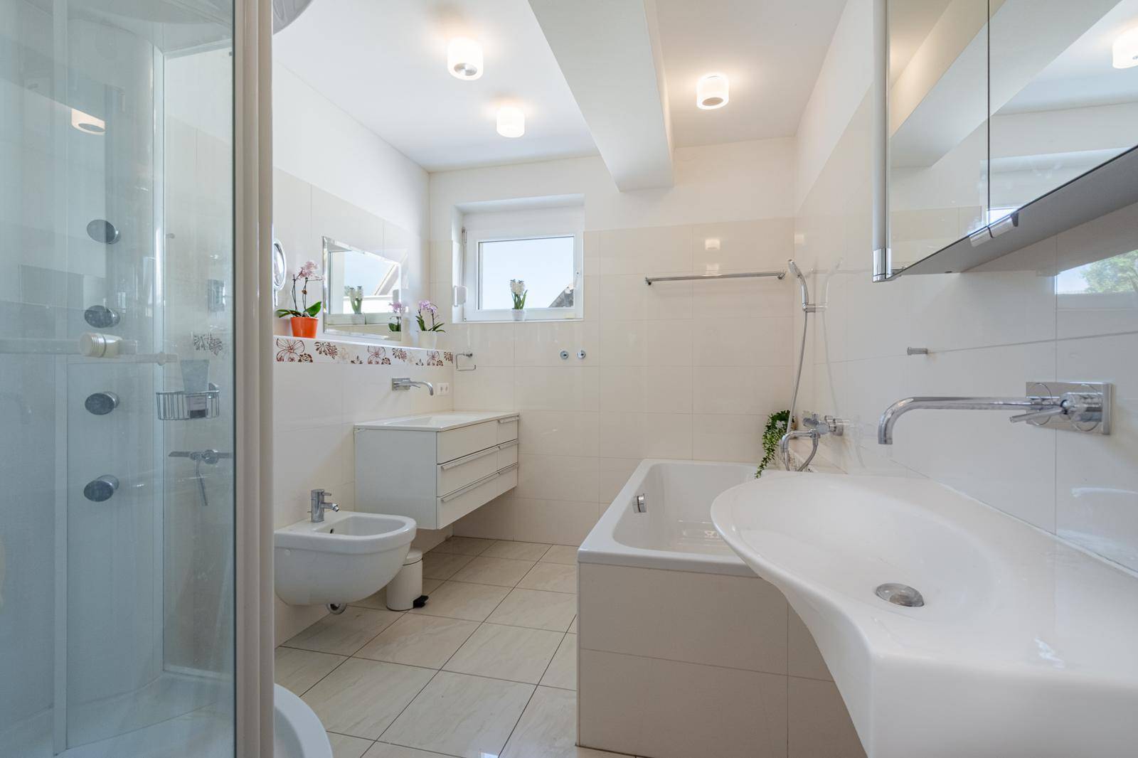 Modernes Badezimmer mit Dusche, Badewanne, Bidet und Doppelwaschbecken in Weiß gehalten.