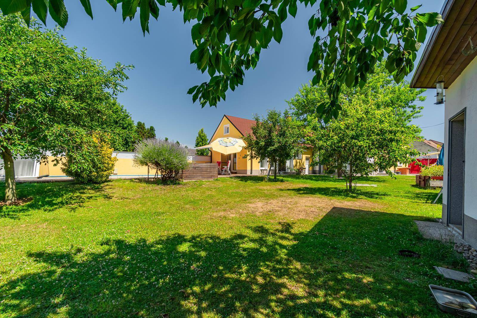 Großer, gepflegter Garten mit Rasenfläche, Bäumen und Blick auf das Haus im Hintergrund.