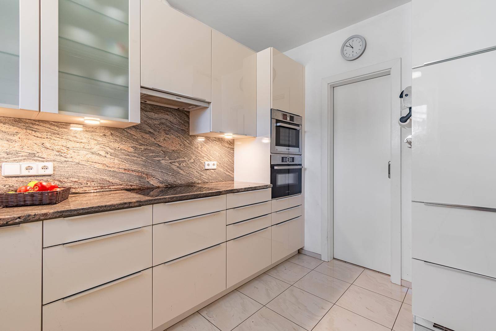 Moderne Küche mit beigen Hochglanzfronten, Granitarbeitsplatte und integrierten Einbaugeräten.