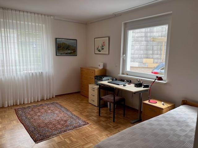 Schlafzimmer mit Einzelbett, Schreibtisch und Blick auf die Umgebung durch das Fenster.