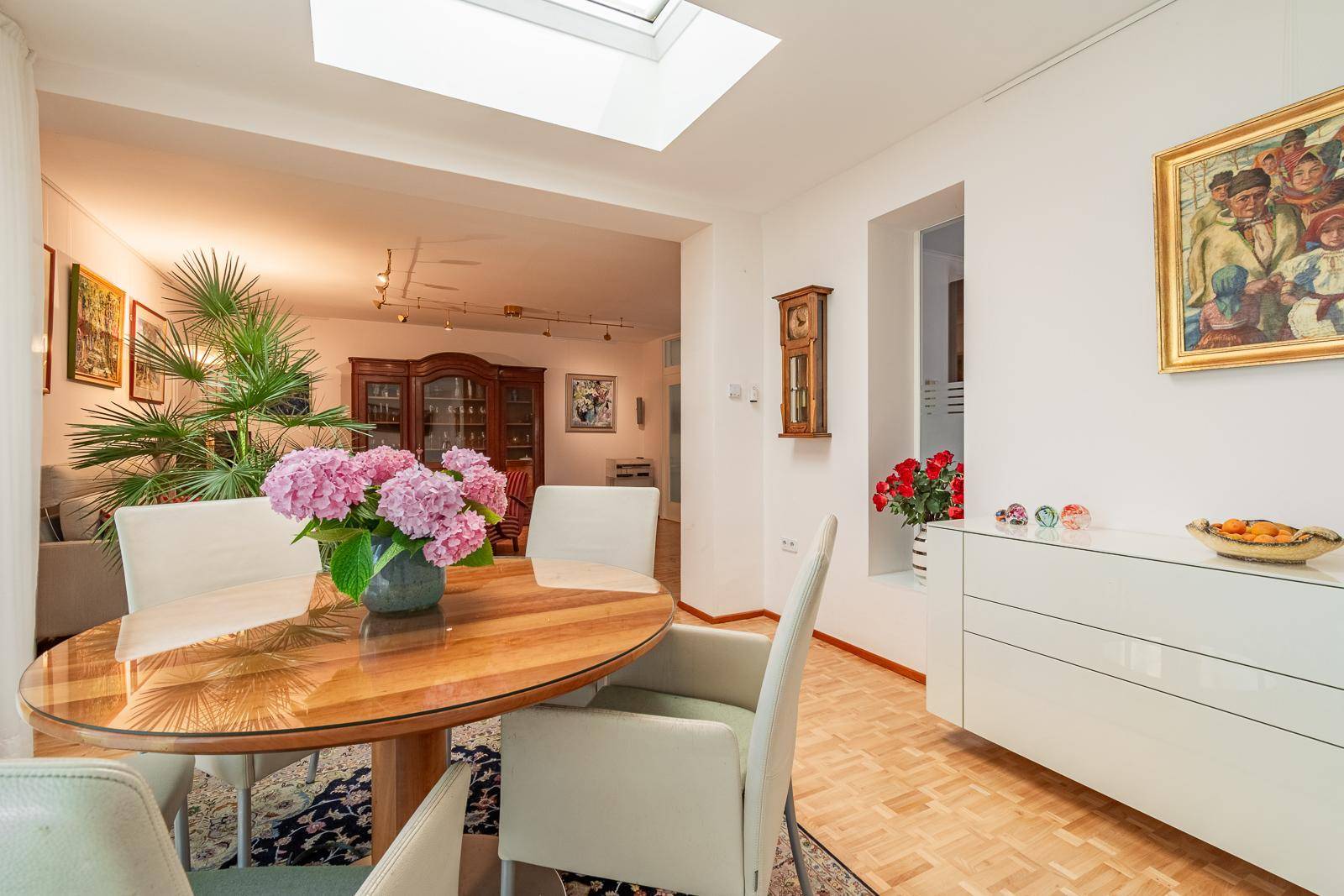 Essbereich mit Holztisch, hellen Stühlen und offenem Übergang zum Wohnzimmer mit Pflanzen.