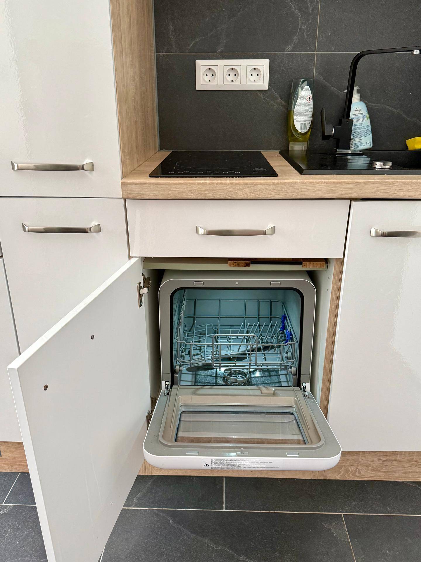 Detailansicht der Küchenzeile mit geöffnetem Geschirrspüler und Induktionskochfeld.