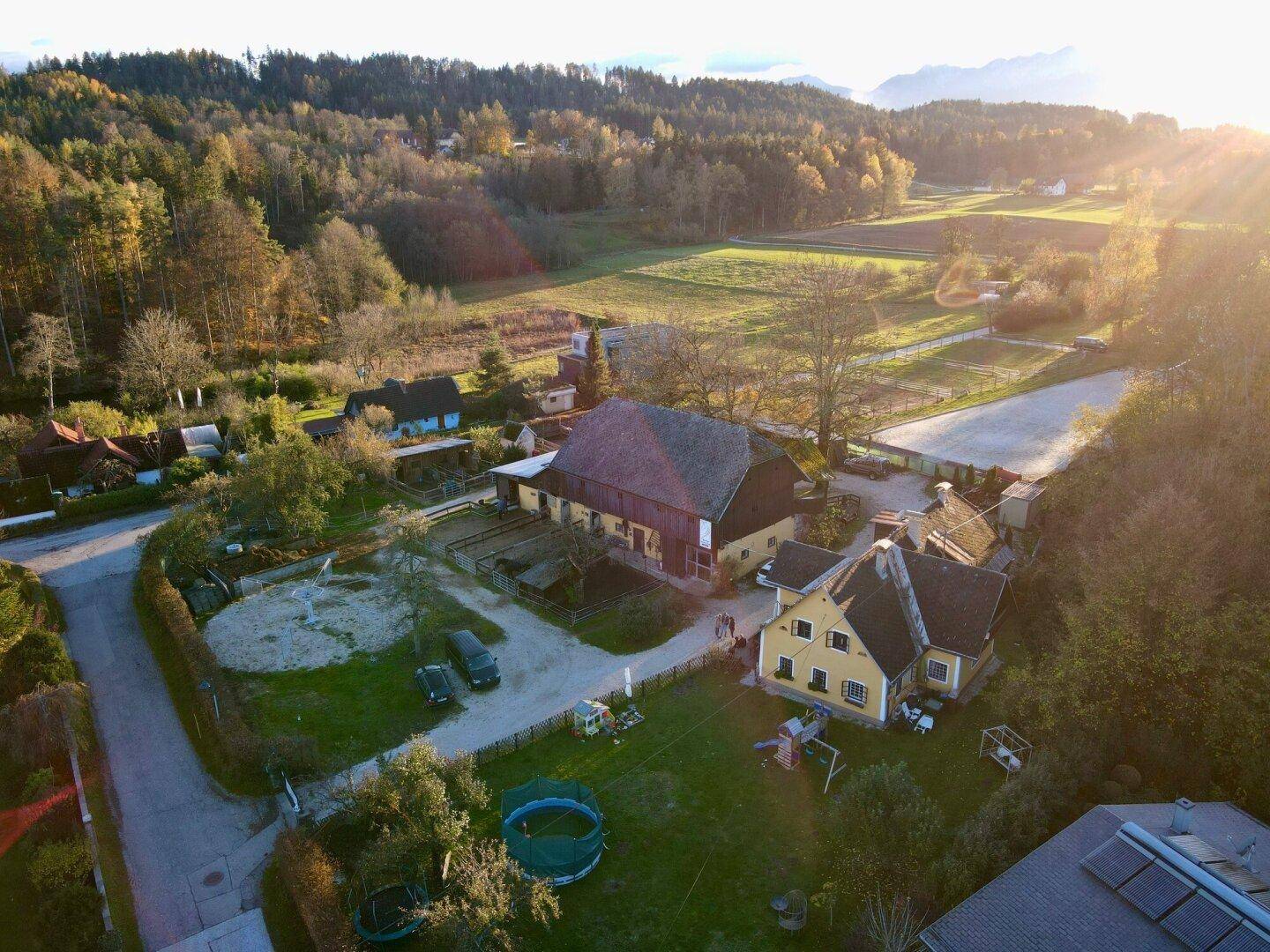 Weitläufige Luftaufnahme des Anwesens mit ländlicher Umgebung und Bergen im Hintergrund bei Sonnenuntergang.